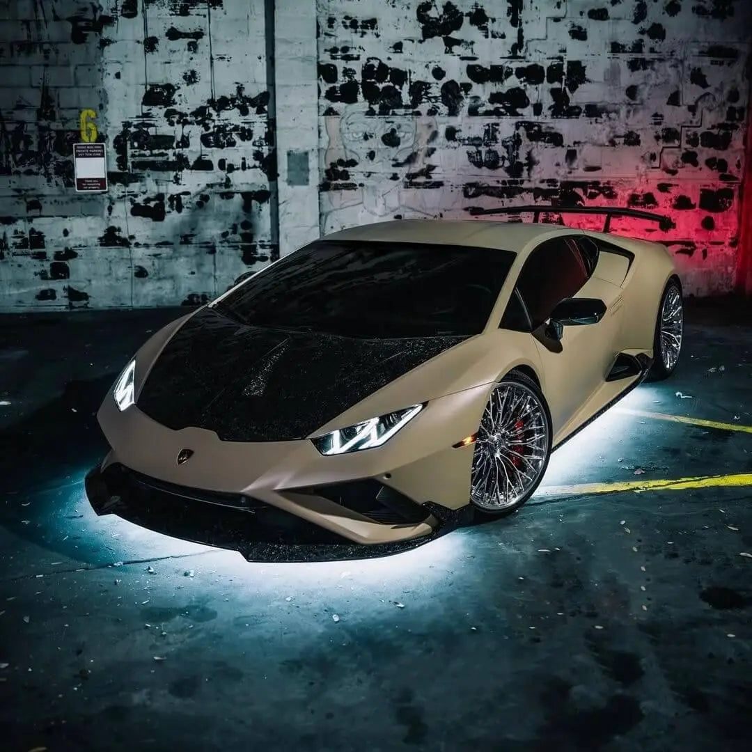 Matte Sand Lamborghini Huracán with white LED underglow, parked in front of a gritty urban wall.