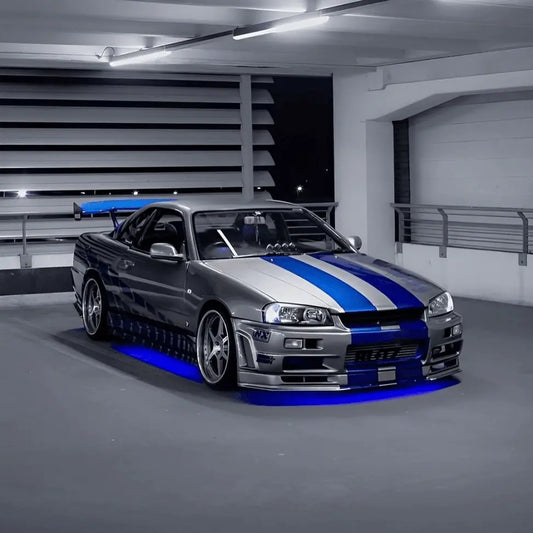 Nissan Skyline R34 parked in a garage with vibrant blue LED underglow lighting installed underneath.