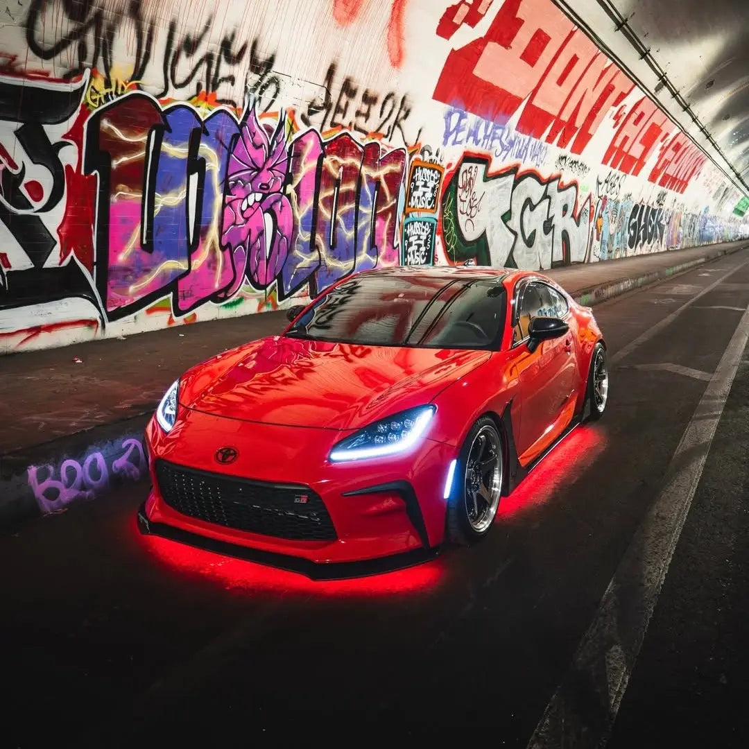 Red sports car with Underglow LED lighting parked in a tunnel with graffiti walls.
