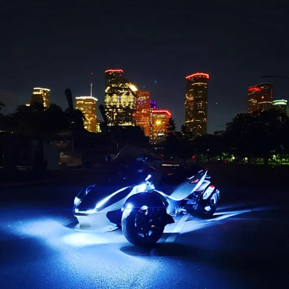 Three-wheeled motorcycle with bright blue Underglow LED lighting against a city skyline at night.