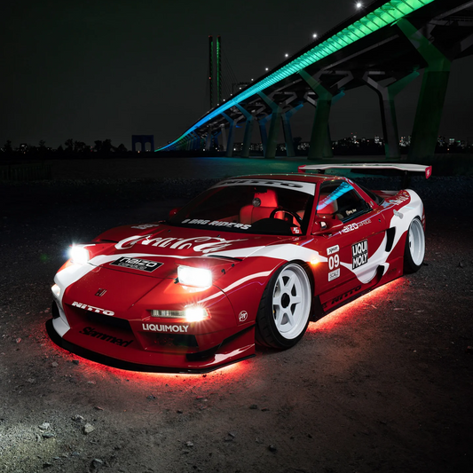 Red modified sports car with bright red LED underglow lighting parked at night near a bridge.