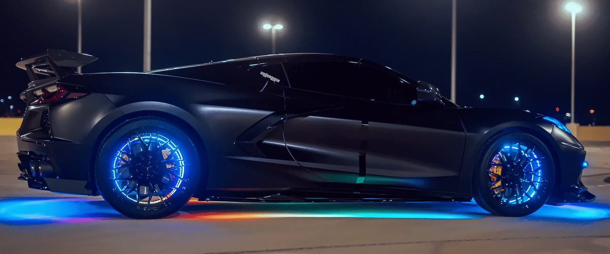 Black Corvette C8 with blue LED wheel ring lights and rainbow underglow at night